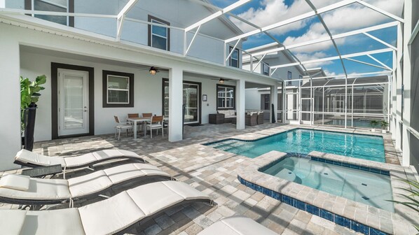 A modern outdoor pool area with lounge chairs, a seating area, and a glass-enclosed structure.