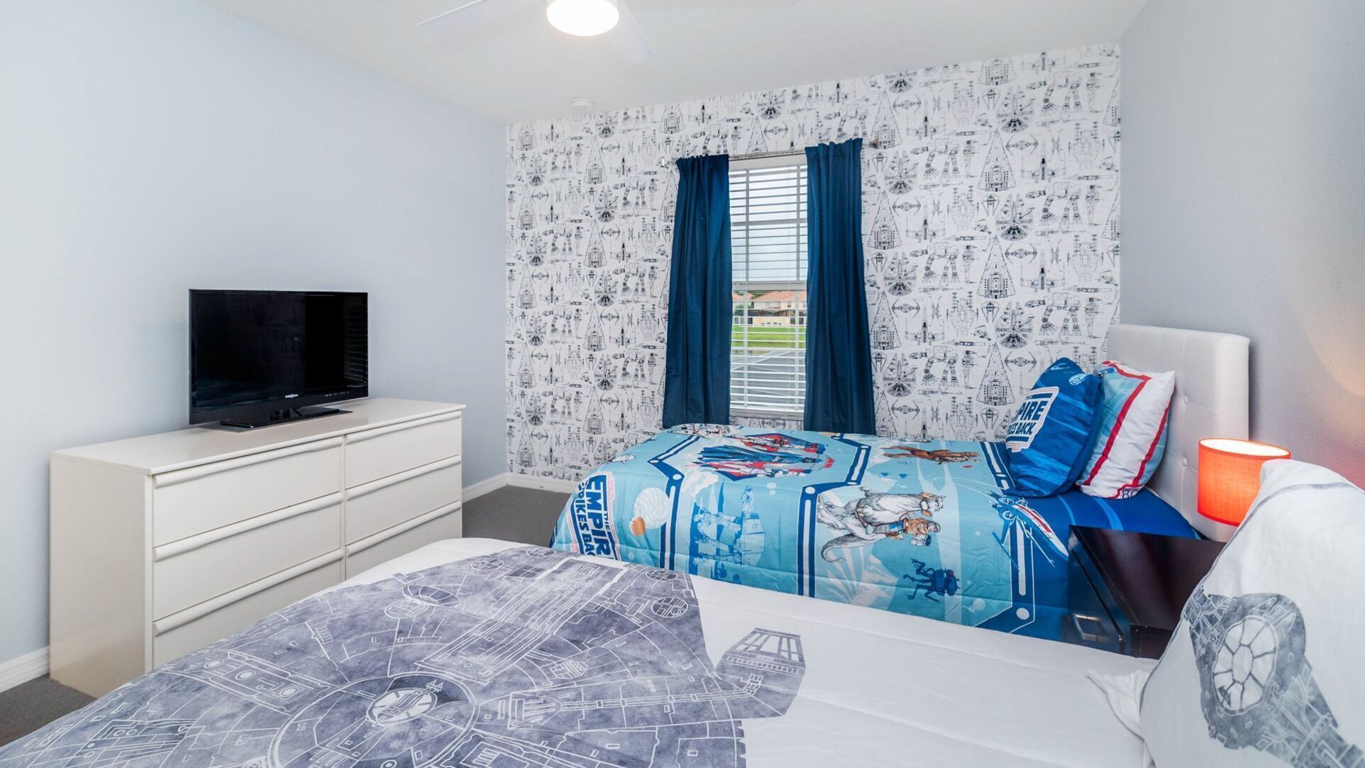 Une chambre à coucher avec un lit, un téléviseur posé sur une commode et une fenêtre avec des rideaux.