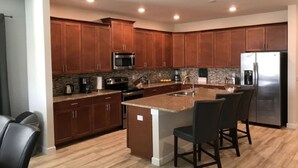 Una cocina moderna con armarios de madera, encimeras de granito, electrodomésticos de acero inoxidable y una isla central con taburetes de bar.