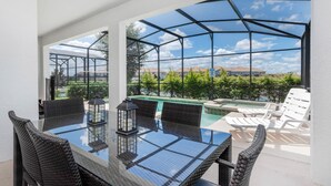 Un espacio al aire libre cubierto con una mesa de vidrio y sillas de mimbre, con vistas a una piscina y follaje.