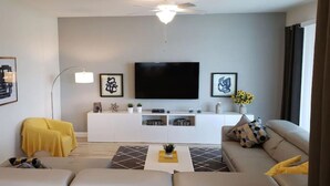 Una sala de estar moderna con un televisor de pantalla plana, un mueble blanco para entretenimiento y un ventilador de techo.