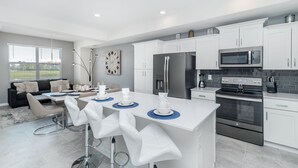 Een moderne keuken met witte kastjes, roestvrijstalen apparatuur en een centraal eiland met barkrukken.