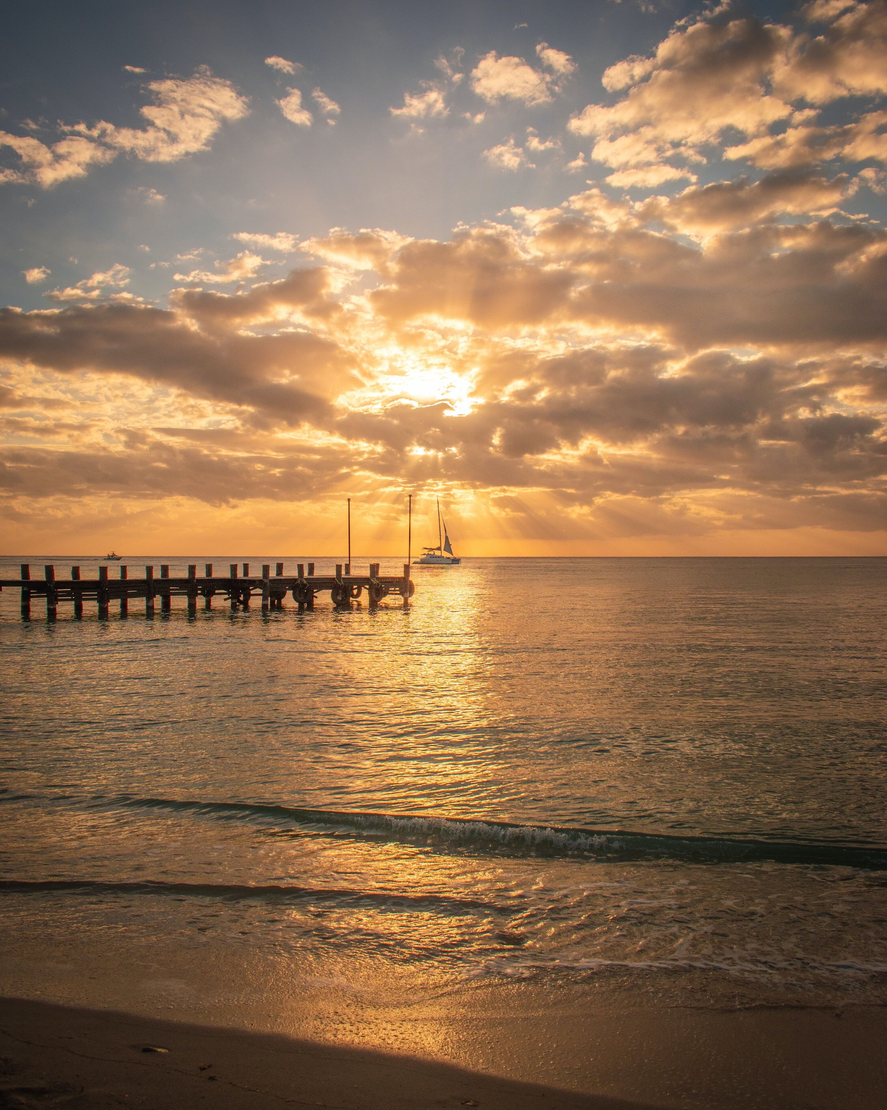 Un coucher de soleil sur une mer calme, avec une jetée qui s’avance dans l’eau.