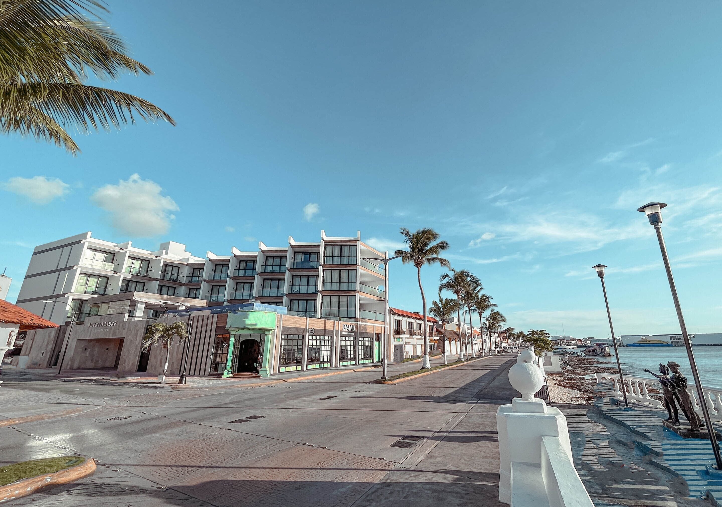 A modern hotel with a multi-story structure, a beachfront view, and a pedestrian walkway along the water.