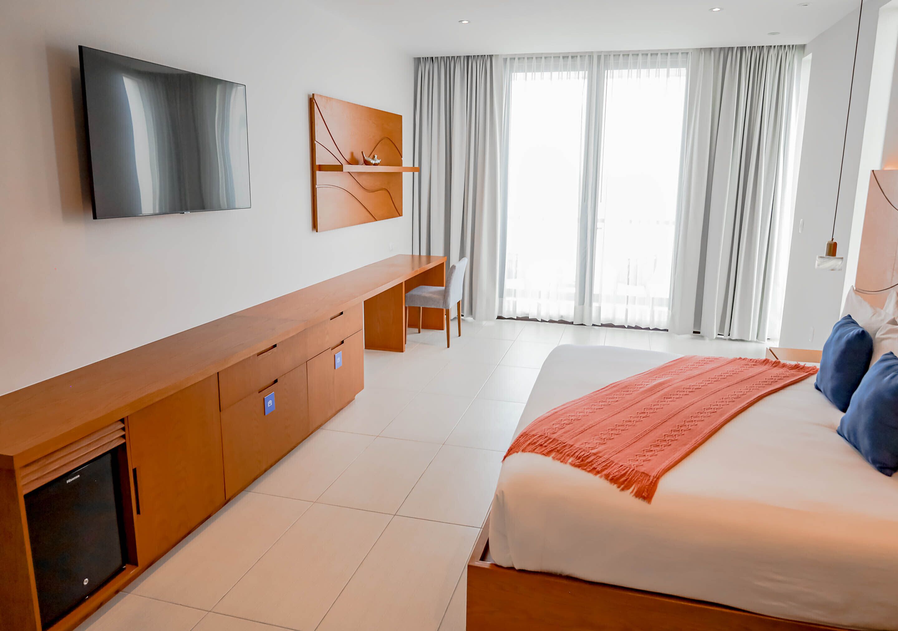 Une chambre d’hôtel moderne avec un grand lit, un téléviseur fixé au mur, un bureau et une chaise.
