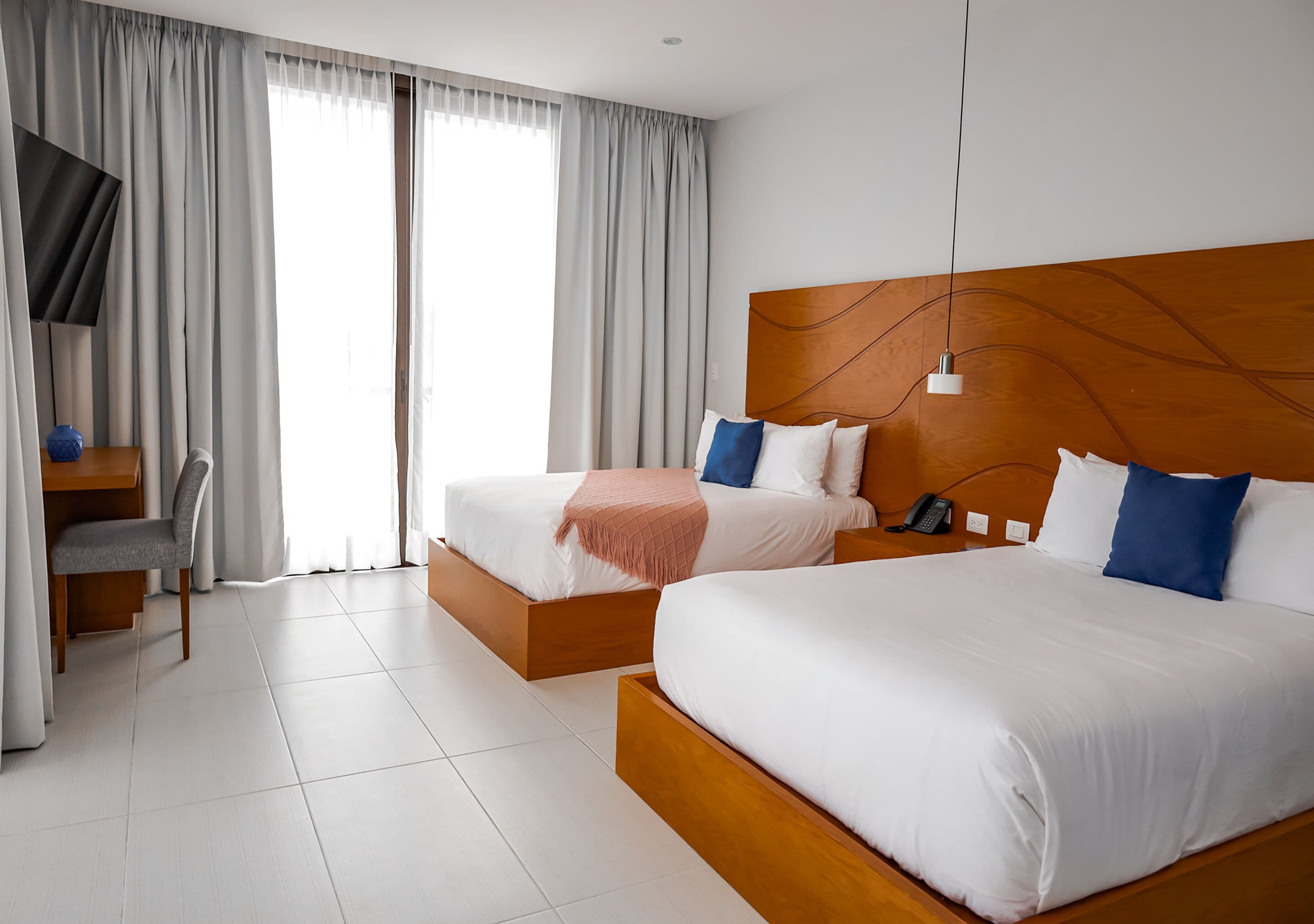 A hotel room with two beds, a TV, and a desk with a chair.