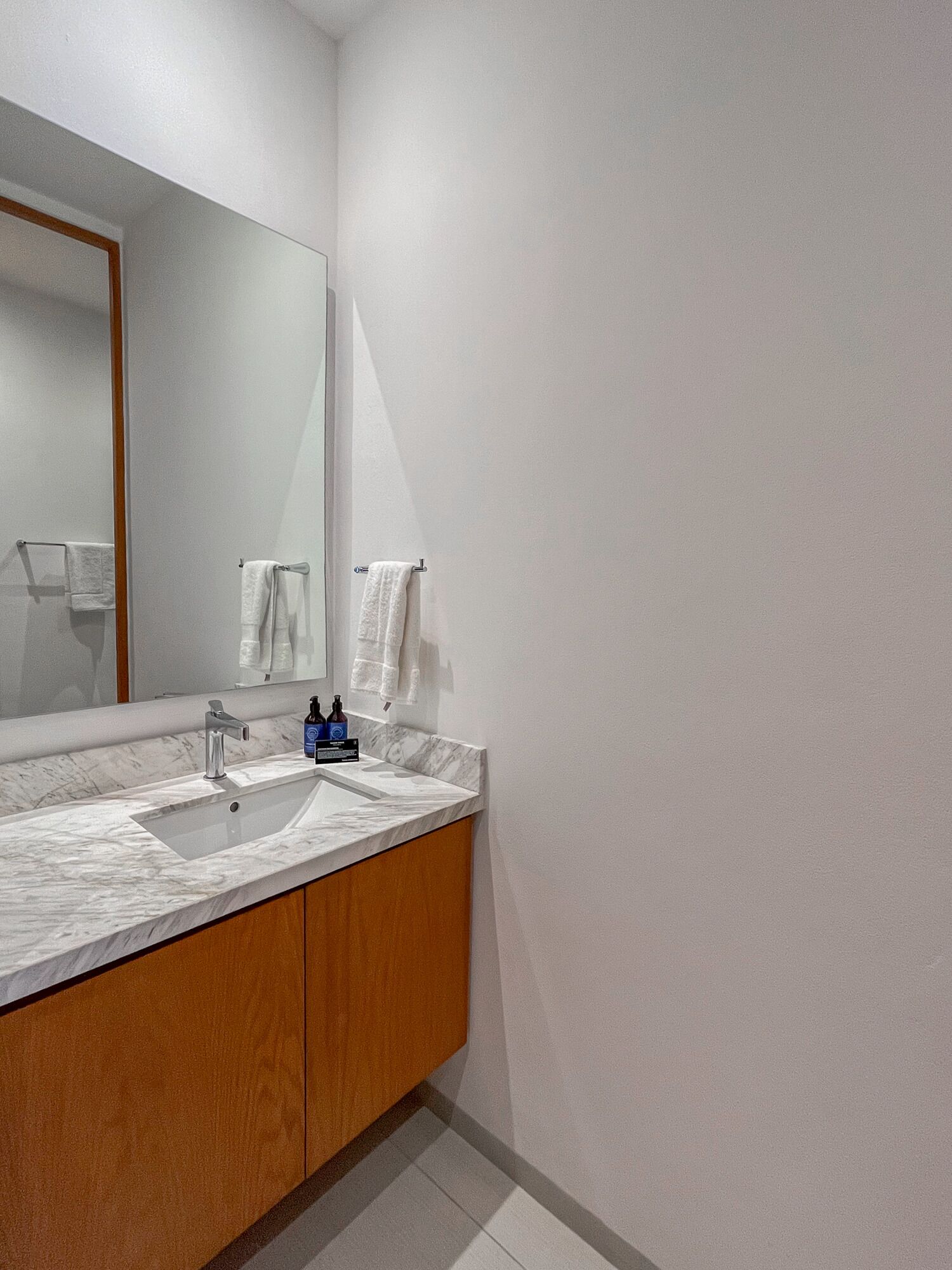 A modern bathroom with a marble sink, wooden cabinets, and a large mirror.