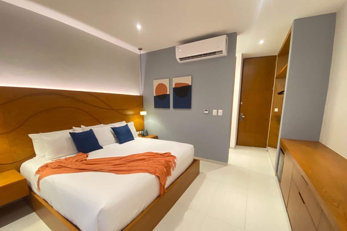 Quarto de hotel moderno com uma cama grande, cabeceira de madeira, mesa de cabeceira, ar condicionado e um banco de madeira.
