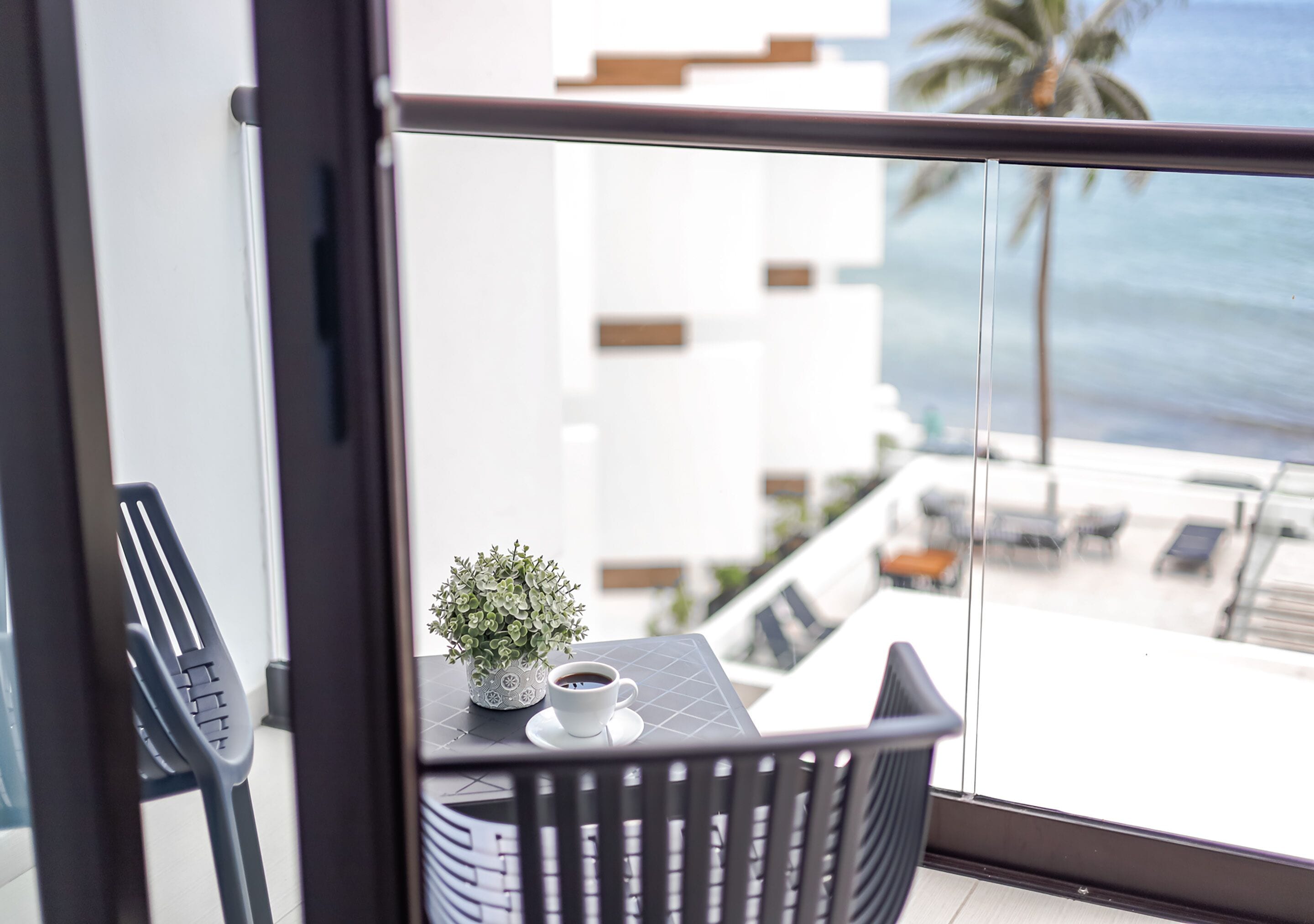 Ein Balkon mit Tisch, Stühlen, einer Topfpflanze und einer Kaffeetasse.