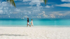 A couple walking on a beach with a boat in the background.