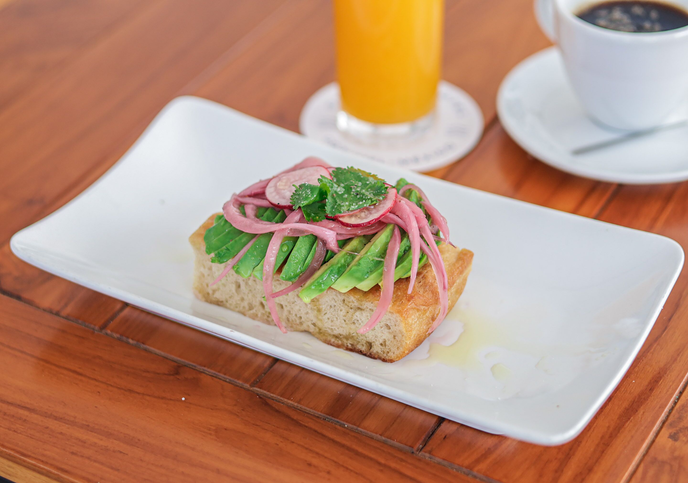 Un plato de desayuno con un sándwich, un vaso de zumo de naranja y una taza de café sobre una mesa de madera.