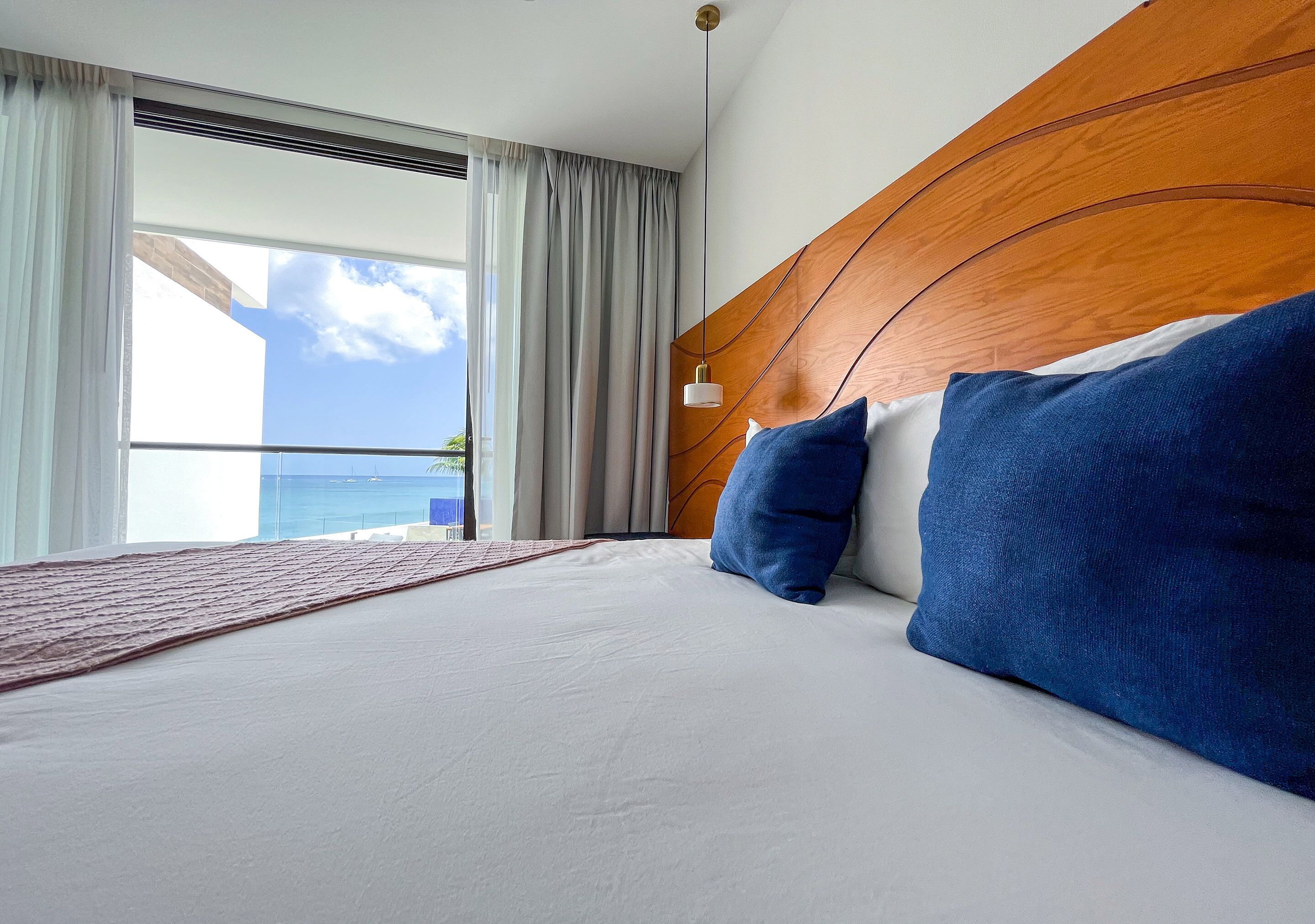 A hotel room with a large bed, a wooden headboard, and a view of the ocean through a large window.