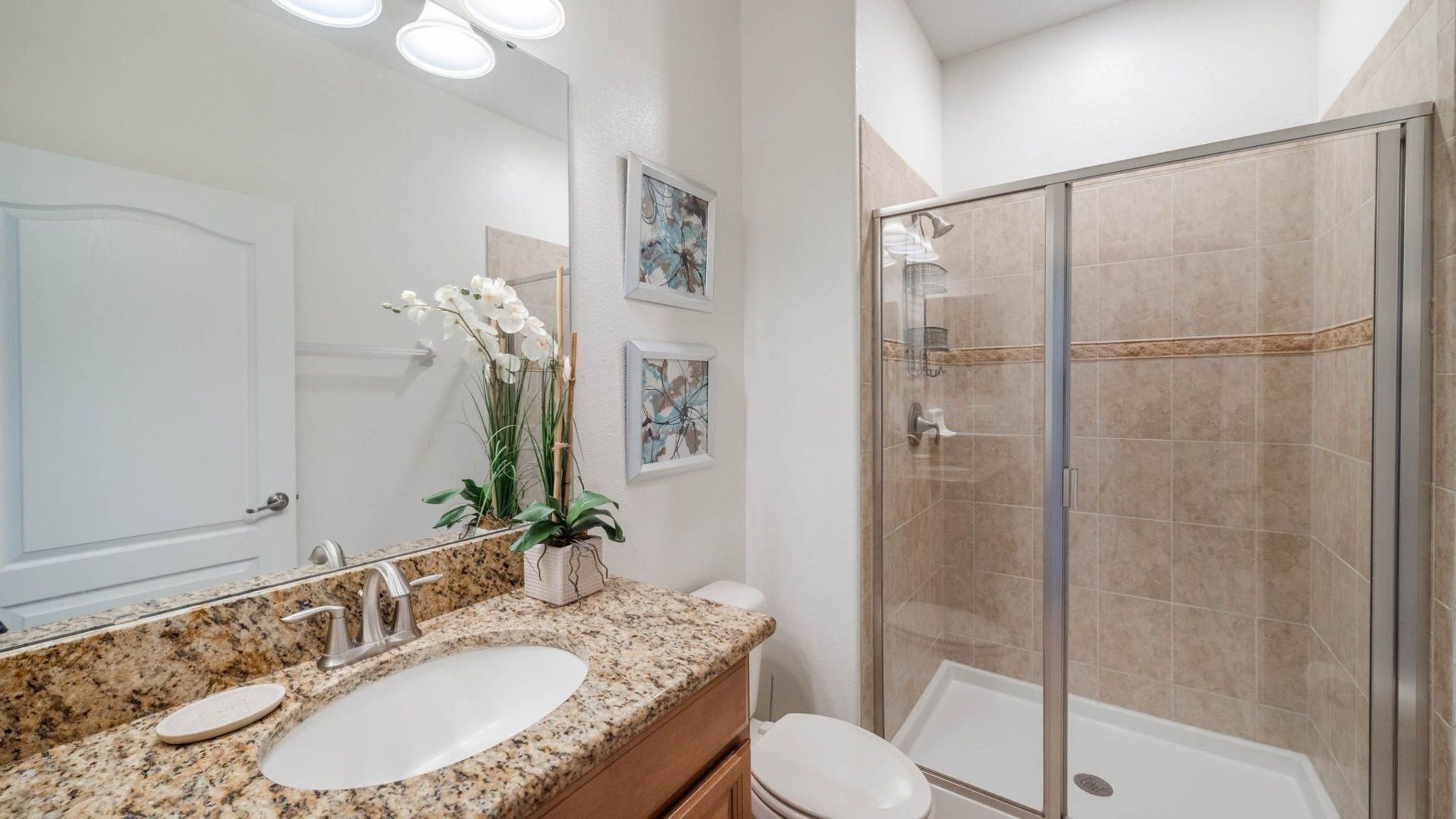 A bathroom with a granite countertop, a white sink, a glass shower enclosure, and a toilet.