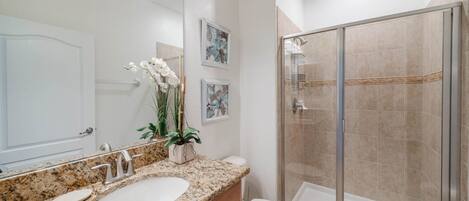 A bathroom with a granite countertop, a white sink, a glass shower enclosure, and a toilet.