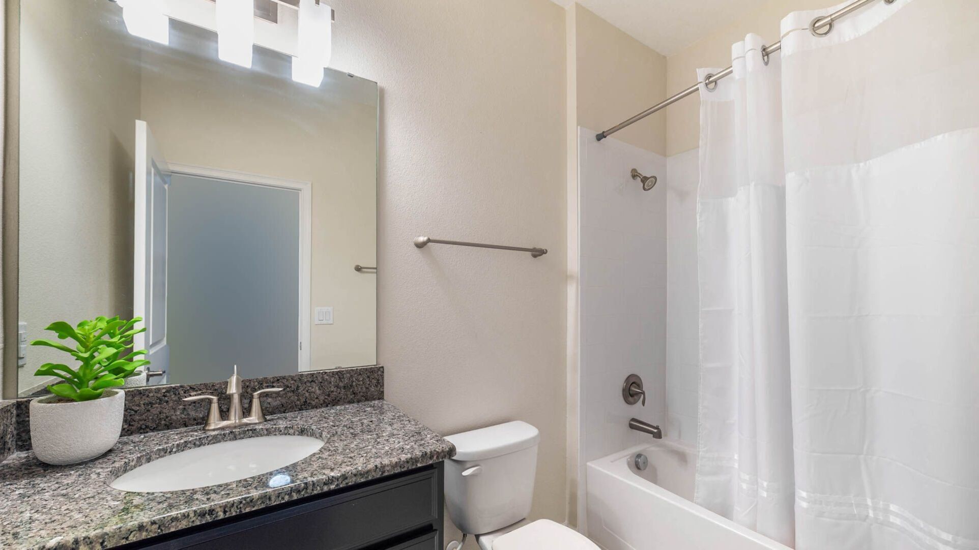A bathroom with a granite countertop sink, a toilet, a shower with a glass door, and a mirror with a light above it.