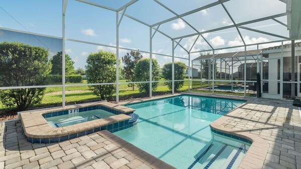 En swimmingpool med et spabad, omgivet af en overdækket terrasse med udsigt over et grønt landskab.