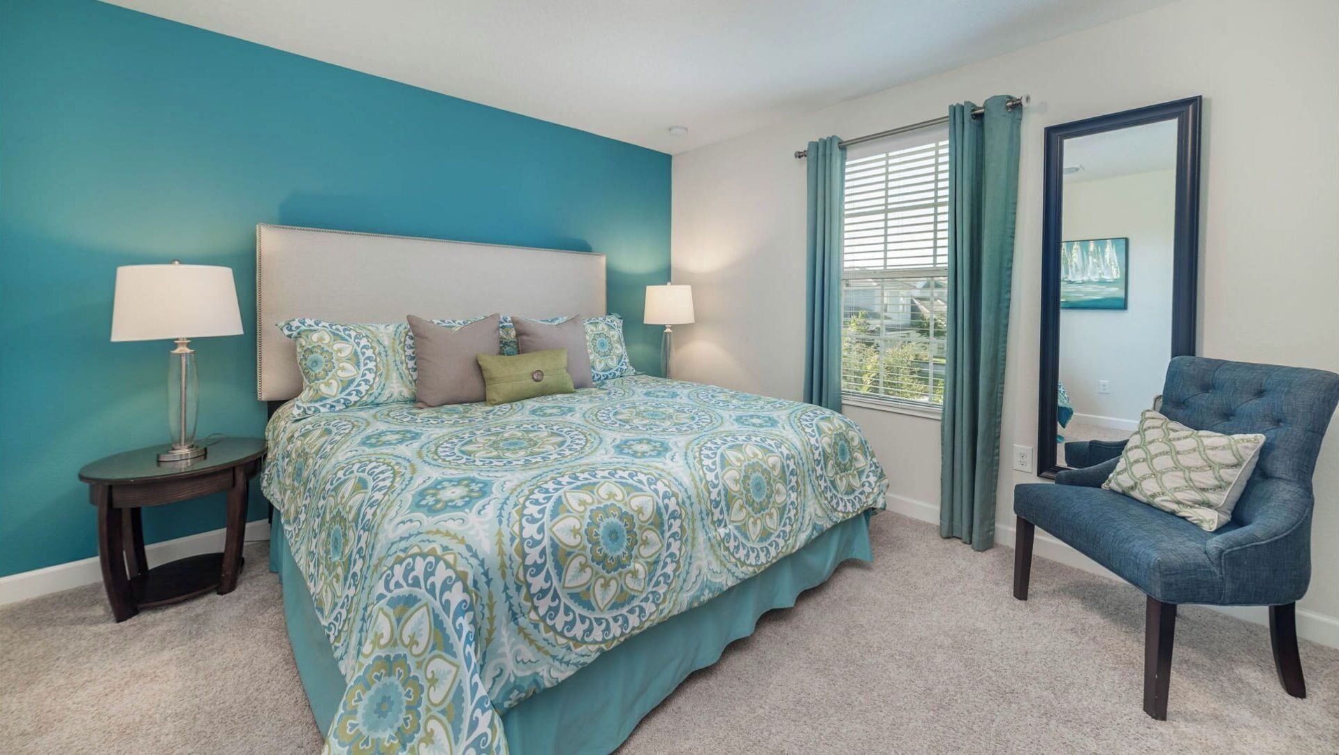 A bedroom with a large bed, two bedside tables, a chair, a window with curtains, and a mirror.