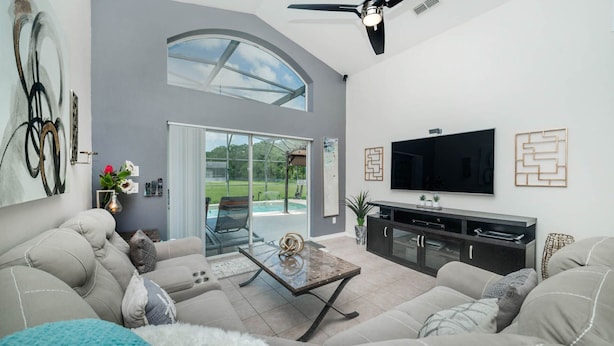 A modern living room with a large TV, comfortable seating, a glass door leading to a patio, and a ceiling fan.
