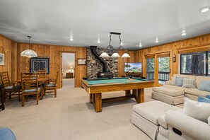 A pool table in a room with wooden walls, a stone fireplace, and a sofa.