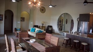 Amplia sala de estar con mesa de comedor, mobiliario de mimbre y cocina moderna con electrodomésticos de acero inoxidable.
