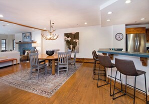 A modern kitchen with a built-in refrigerator, a dining area with a wooden table and chairs, and a large chandelier. - Charlie Rentz: Ski-In/Out in Heart of Beaver Creek, Ice Rink Views, Walk Everywhere (Beaver Creek)