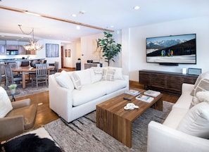 A modern living room with a white sofa, wooden coffee table, and a TV mounted on the wall. - Charlie's Slopeside: Ski-In/Out in Heart of Beaver Creek, Ice Rink Views, Walk Everywhere (Beaver Creek)