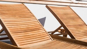 A wooden deck with lounge chairs, a white railing, and a building with balconies in the background. - ☀️ ❤️ Watch Sunsets over the Rooftops at an Old Town Penthouse (Albufeira)