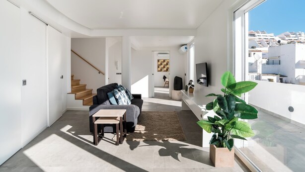 A modern living room with a sofa, coffee table, and a large window offering a view of buildings. - ☀️ ❤️ Watch Sunsets over the Rooftops at an Old Town Penthouse (Albufeira)