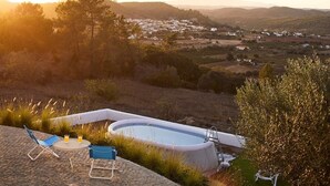 Ein Pool mit Liegestuhl und Tisch, umgeben von Gras und Bäumen mit Blick auf ein Tal.