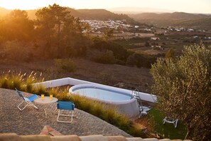 Une piscine avec un fauteuil de relaxation et une table, entourée de pelouse et d’arbres, et offrant une vue sur une vallée.