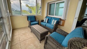 A sunlit patio with wicker furniture, a sliding glass door, and a view of palm trees.