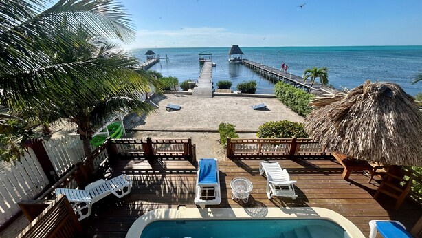 A pool area with lounge chairs and a hot tub, overlooking a beach and pier.