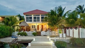 A two-story house with a red roof, a white picket fence, and a wooden dock leading to the water.