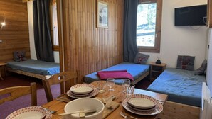 A cozy cabin with two wooden beds, a dining table with plates and cutlery, and a TV mounted on the wall. - La Lauzière-Dessus 27 - Divisible studio on the edge of the slopes, with a terrace facing south (LES AVANCHERS VALMOREL)