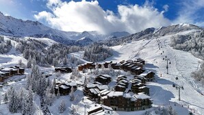 A snow-covered mountain resort with chalet-style buildings, ski slopes, and a clear sky. - La Lauzière-Dessus 27 - Divisible studio on the edge of the slopes, with a terrace facing south (LES AVANCHERS VALMOREL)