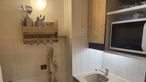 A compact kitchen with a microwave, sink, and wooden cabinets. - La Lauzière-Dessus 27 - Divisible studio on the edge of the slopes, with a terrace facing south (LES AVANCHERS VALMOREL)