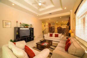 Ein Wohnzimmer mit einer Sofagarnitur, einem Couchtisch, einem Fernseher und einer Treppe, die zu einer oberen Etage führt.