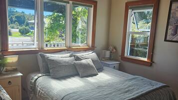 Un dormitorio con una cama grande, dos ventanas, una mesita de noche con una lámpara y techo de madera.