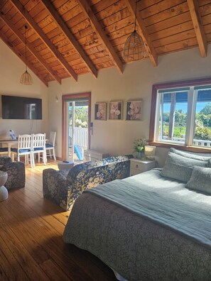 A bedroom with a wooden ceiling, a bed with patterned bedding, a desk with a chair, and a television. - The Blackhouse Cottage (Ruatapu)
