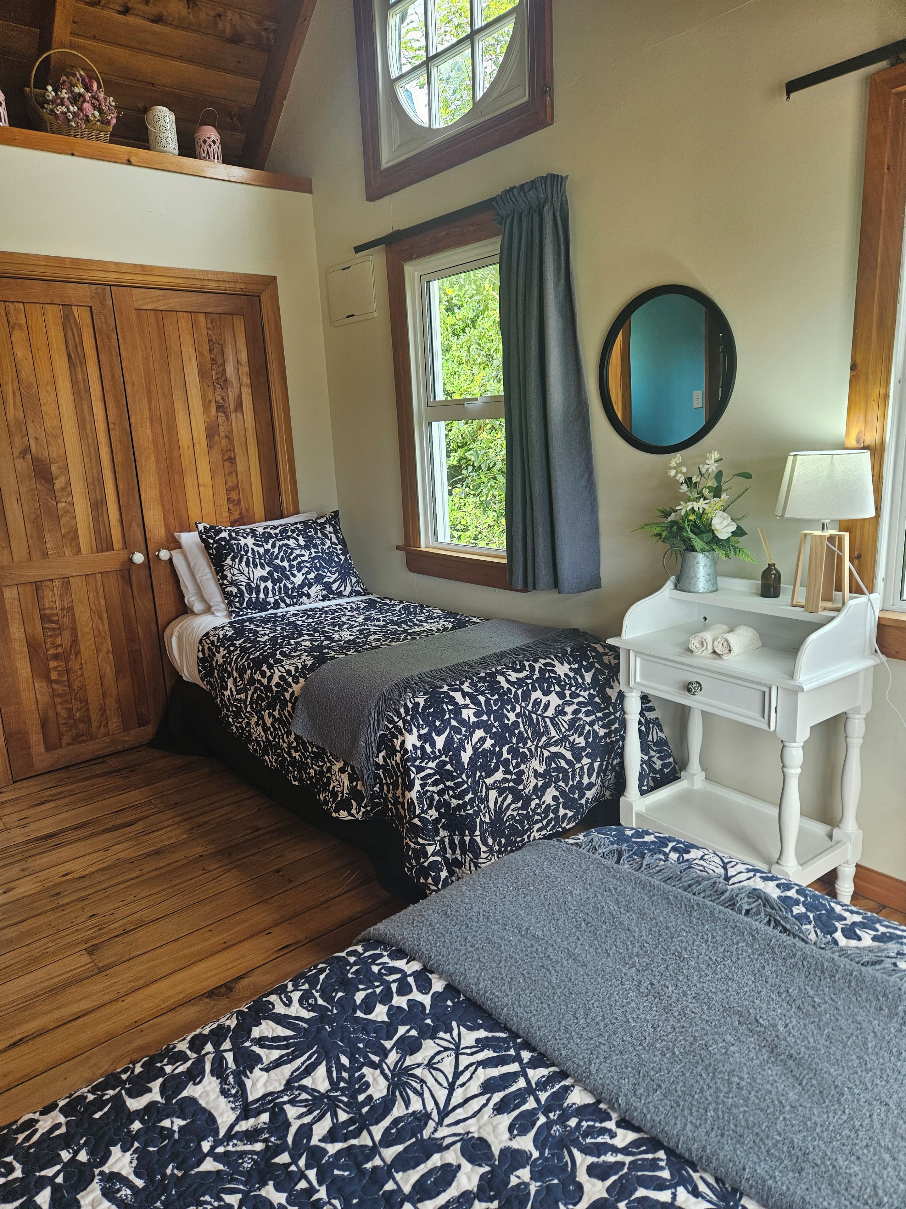 Un dormitorio con un armario de madera, una cama con colcha floral, una mesita de noche con lámpara y una ventana con cortinas.