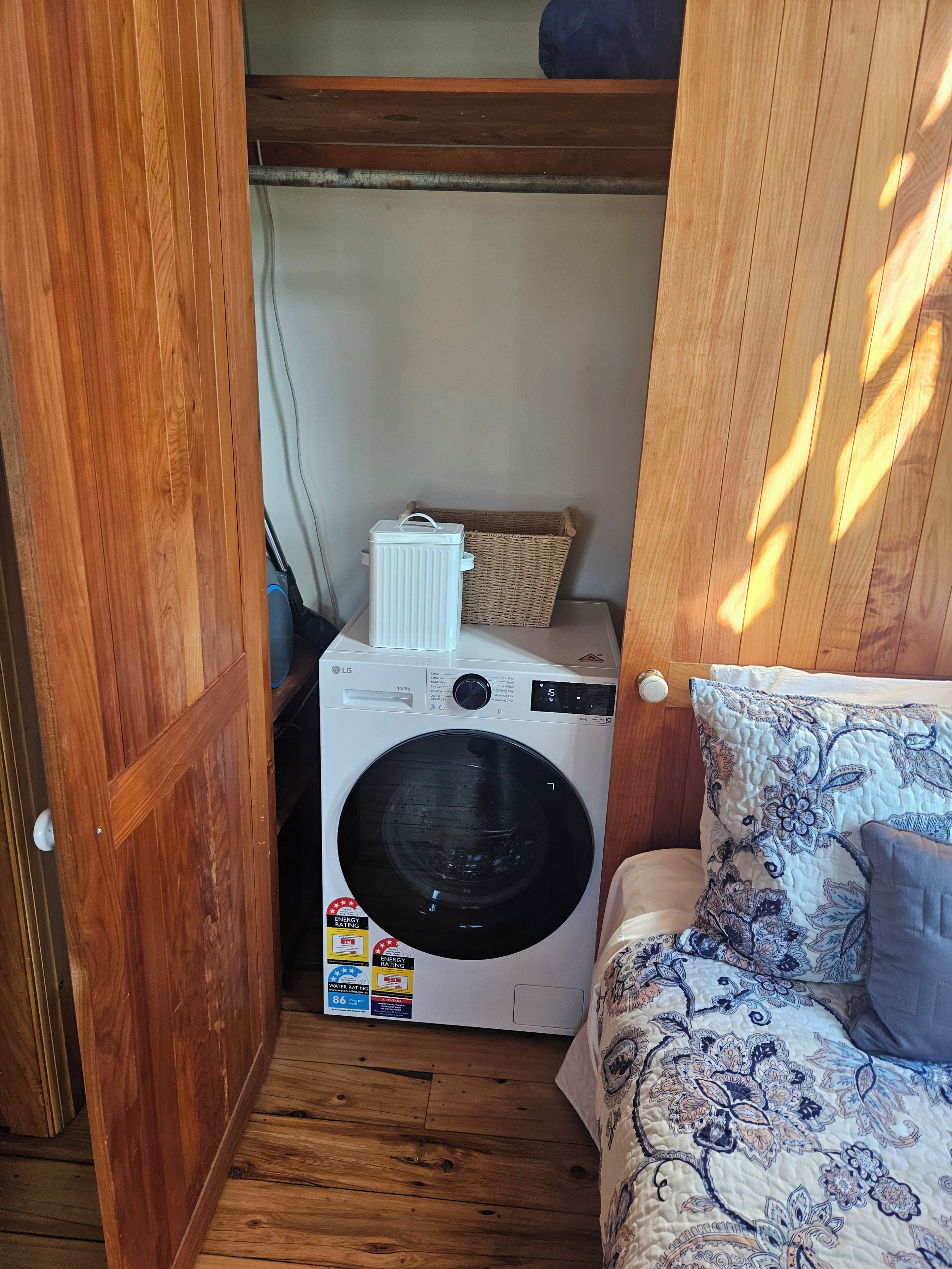 Uma lavanderia compacta com máquina de lavar, cesto de vime e cama com roupa de cama estampada.