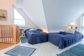 A bedroom with two beds, a wooden crib, and a small table with a lamp. - Apartment house Boddenblick "Himmelkieker" - Spacious apartment on the 2nd floor (Zingst)