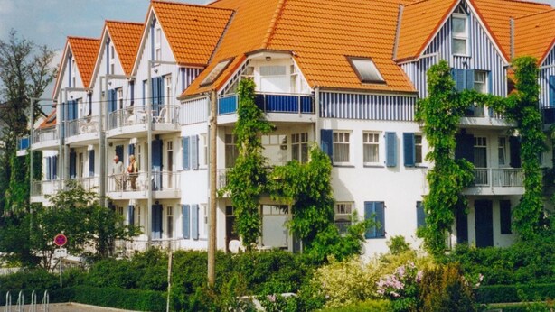 A row of white buildings with orange tiled roofs and blue shutters.