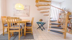 A modern living room with a wooden dining table, chairs, a blue coffee table, a spiral staircase, and a bookshelf filled with books.
