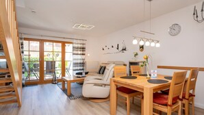 A modern living room with a sofa, dining table, and chairs. There is a staircase leading to an upper floor. - Terraced house with garden, terrace and heated pool in Zingst - vacation park (Zingst)