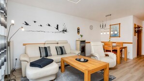 A modern living room with a sofa, armchairs, a wooden coffee table, and a dining table. - Terraced house with garden, terrace and heated pool in Zingst - vacation park (Zingst)