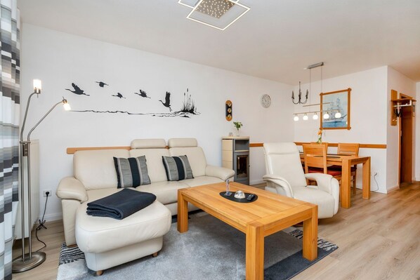 A modern living room with a sofa, armchairs, a wooden coffee table, and a dining table. - Terraced house with garden, terrace and heated pool in Zingst - vacation park (Zingst)