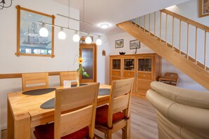 A dining area with wooden furniture, a vase with a flower, and a staircase leading to another level. - Terraced house with garden, terrace and heated pool in Zingst - vacation park (Zingst)