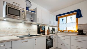 A modern kitchen with white cabinets, stainless steel appliances, a wooden countertop, and a window with blue curtains.