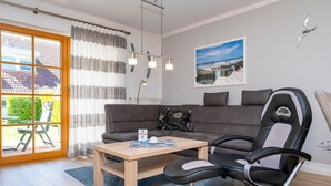 A modern living room with a grey sofa, a black and white chair, a wooden coffee table, and a large window with curtains.